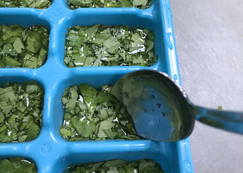 spoon water over herbs in ice cube trays